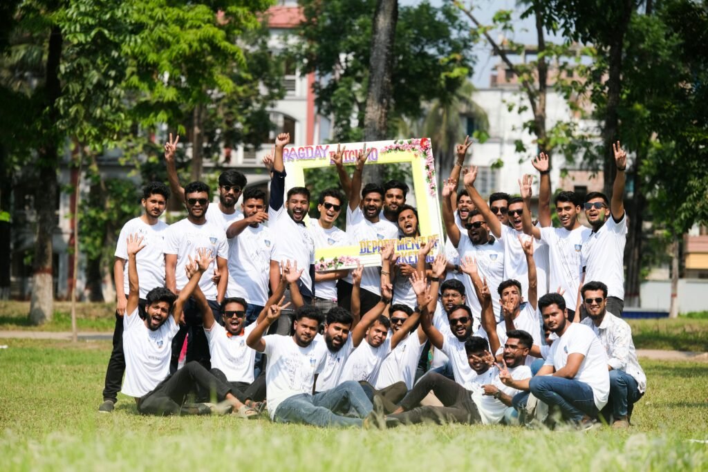 A joyful group of young men celebrating outdoors in a park during summer with a sign and white t-shirts.